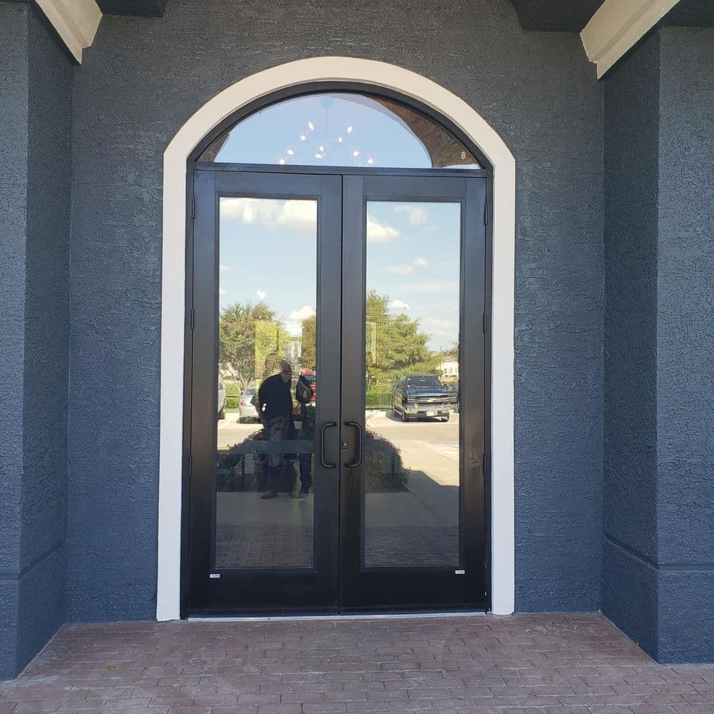 Stylish black double doors with arched window, set against a dark blue wall.