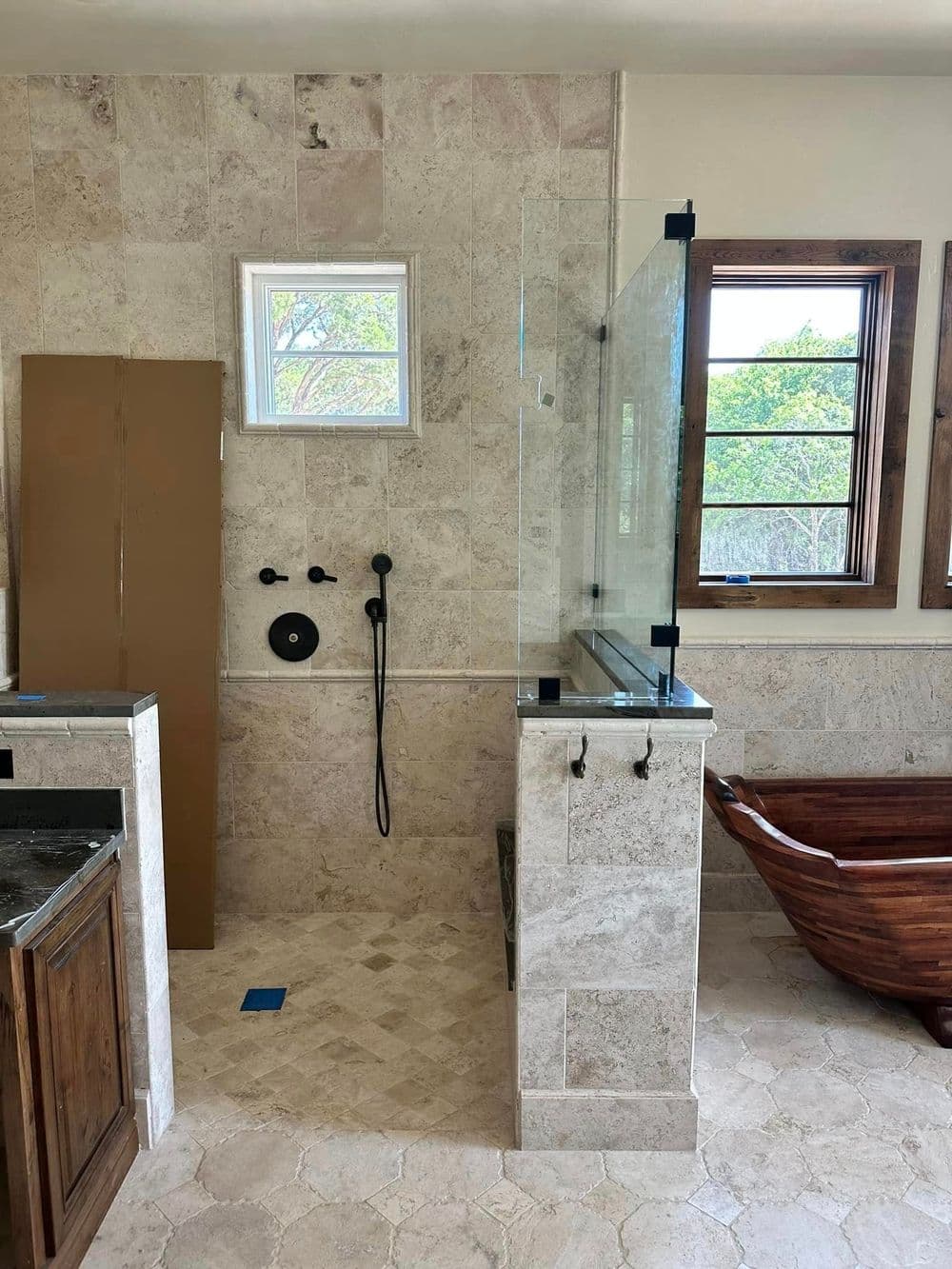 Modern bathroom design featuring a glass shower, wooden tub, and natural stone tiles.