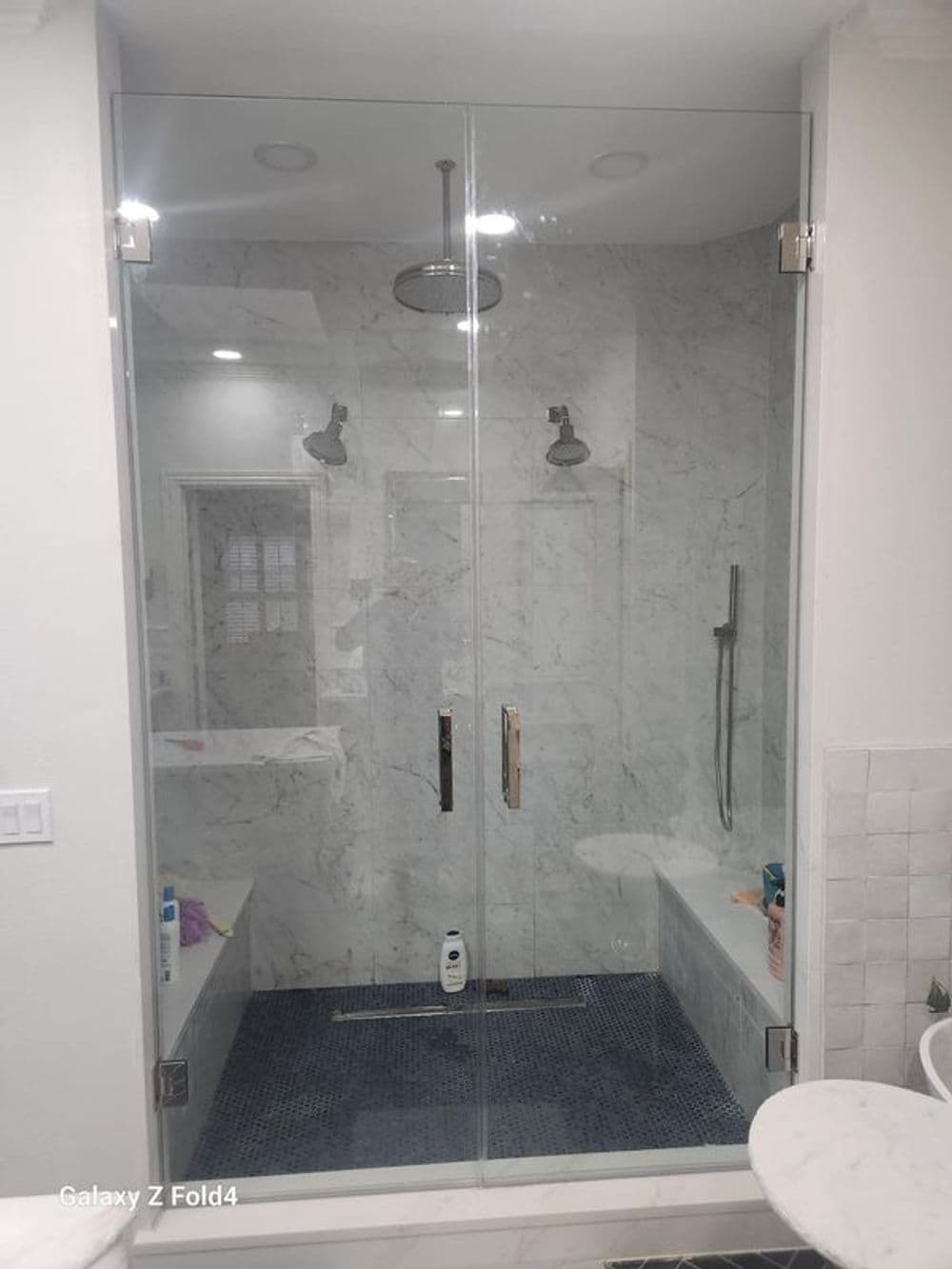Luxurious modern shower with glass doors, marble walls, and stylish blue tile accents.
