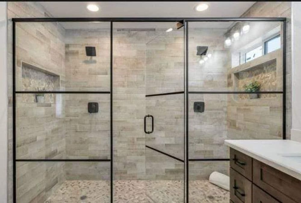 Modern glass shower with black frame, stone tiles, and natural light accentuating the space.