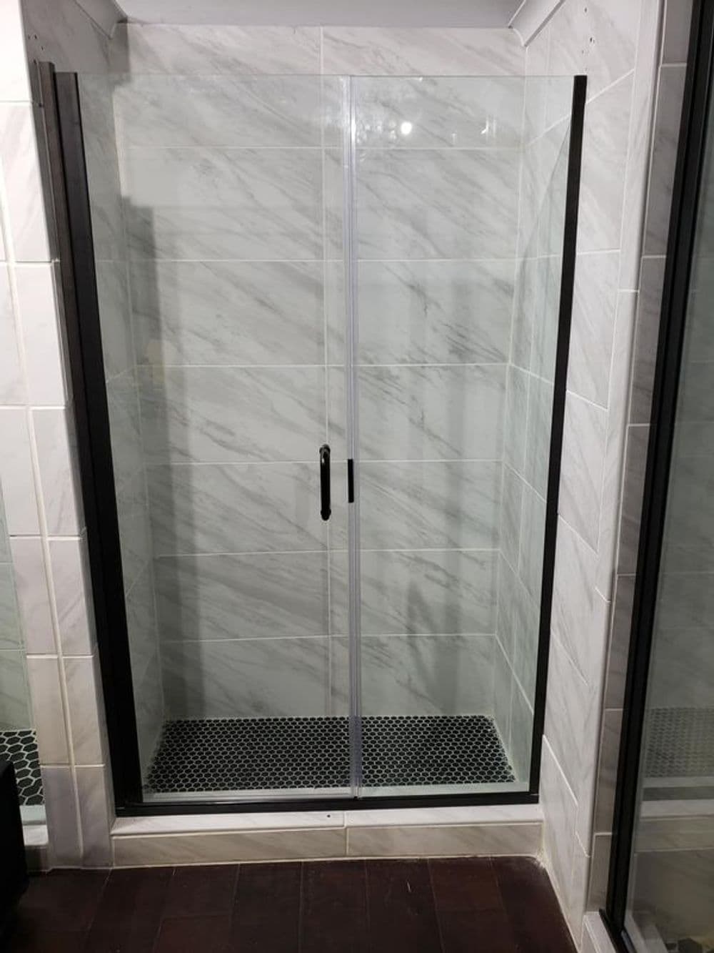 Modern glass shower enclosure with marble walls and black hexagonal floor tiles.