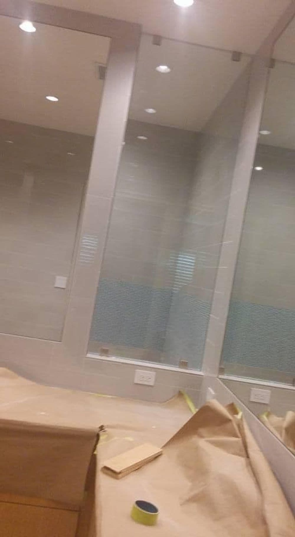 Renovated bathroom with mirrors, blue tile backsplash, and covered surfaces for protection.