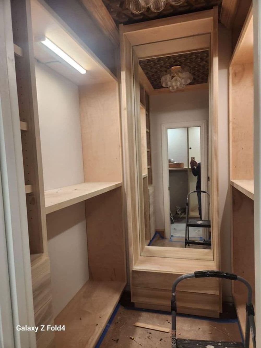 Wooden closet remodel featuring built-in shelves and a mirror, with construction tools visible.