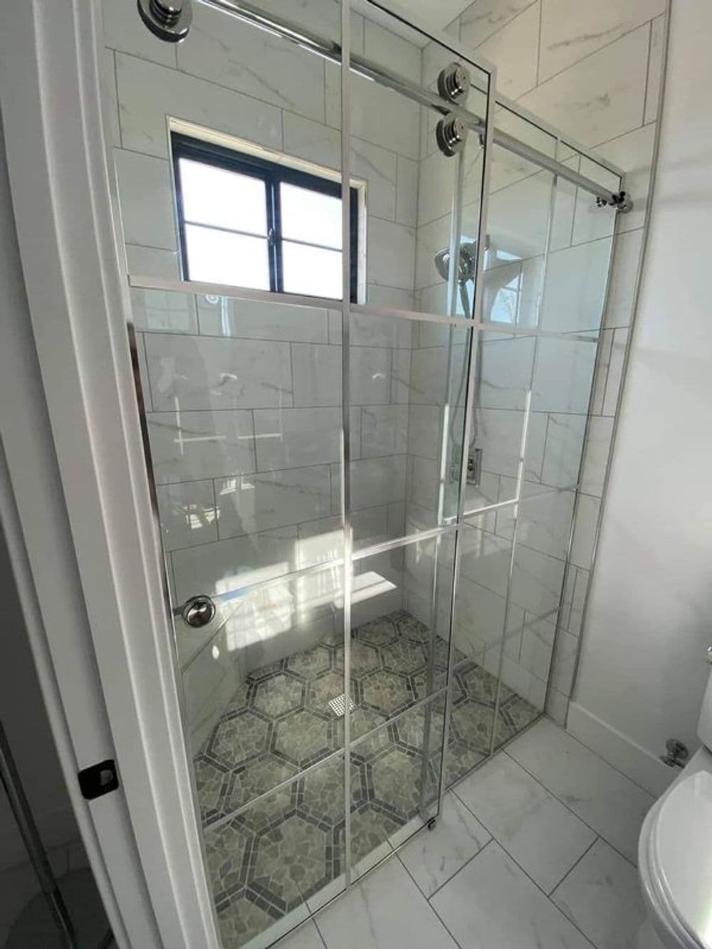 Modern walk-in shower with glass enclosure, marble tiles, and hexagonal patterned floor.
