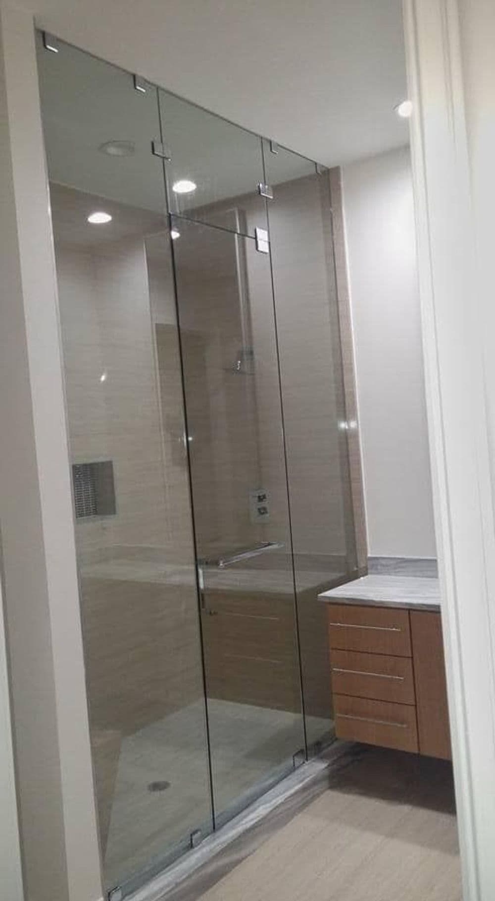 Modern glass shower enclosure in a sleek bathroom with wooden cabinetry and neutral tones.