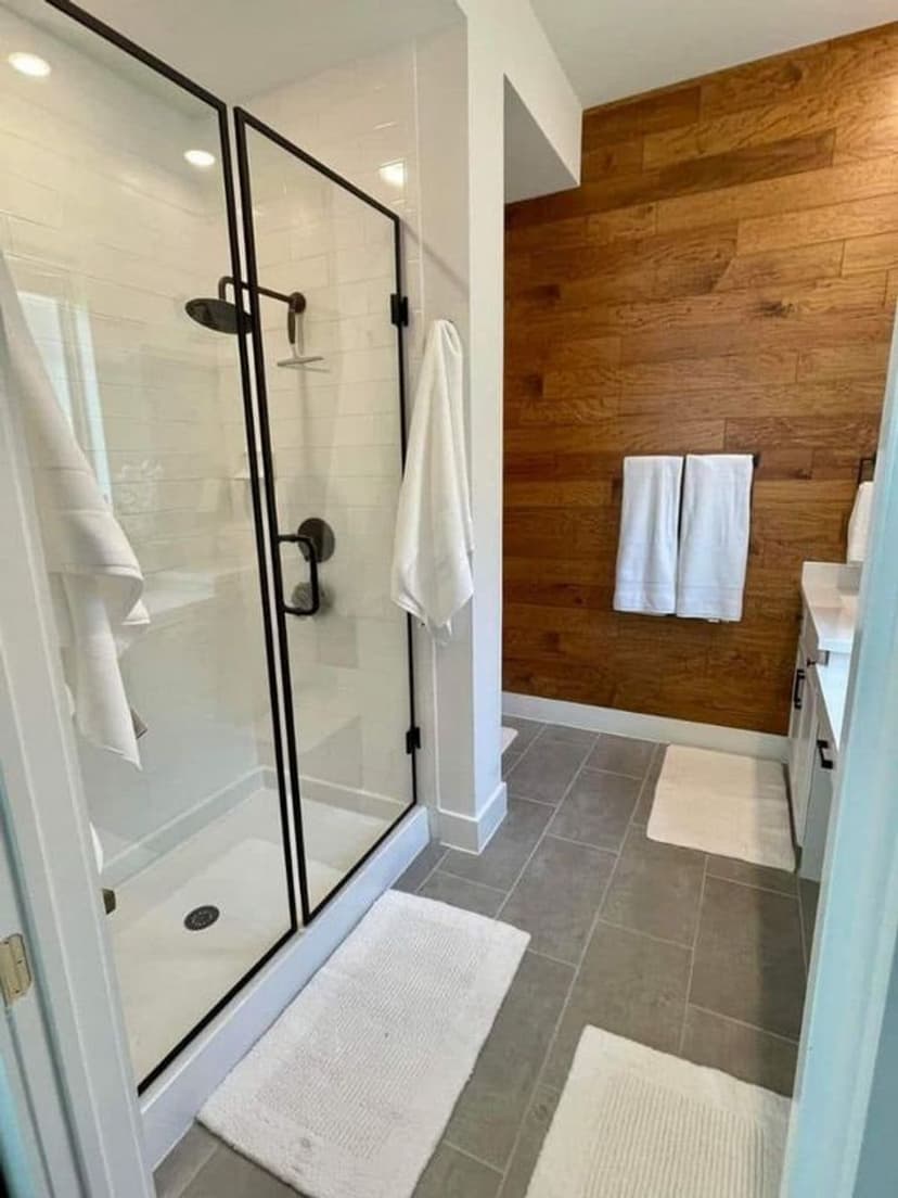 Modern bathroom with glass shower, wooden accent wall, and plush white towels.