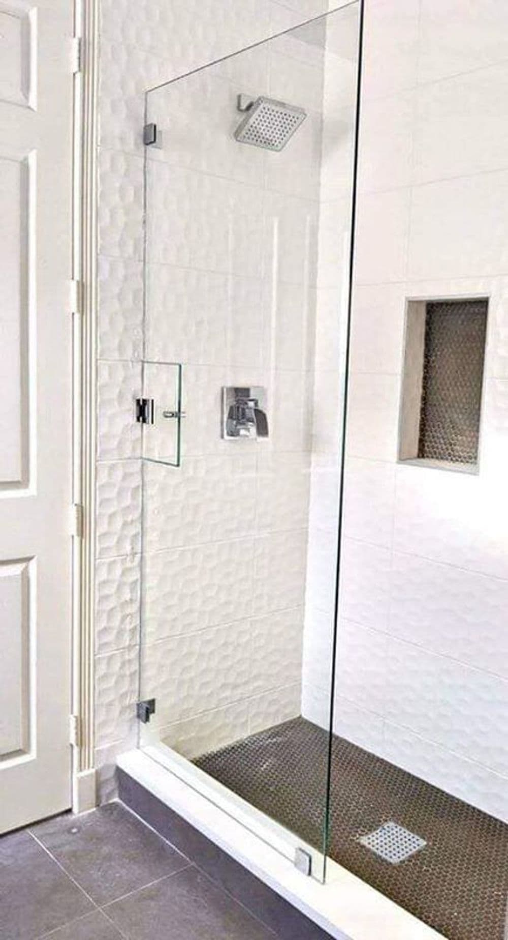 Modern glass shower enclosure with rainfall showerhead and textured tile floor.
