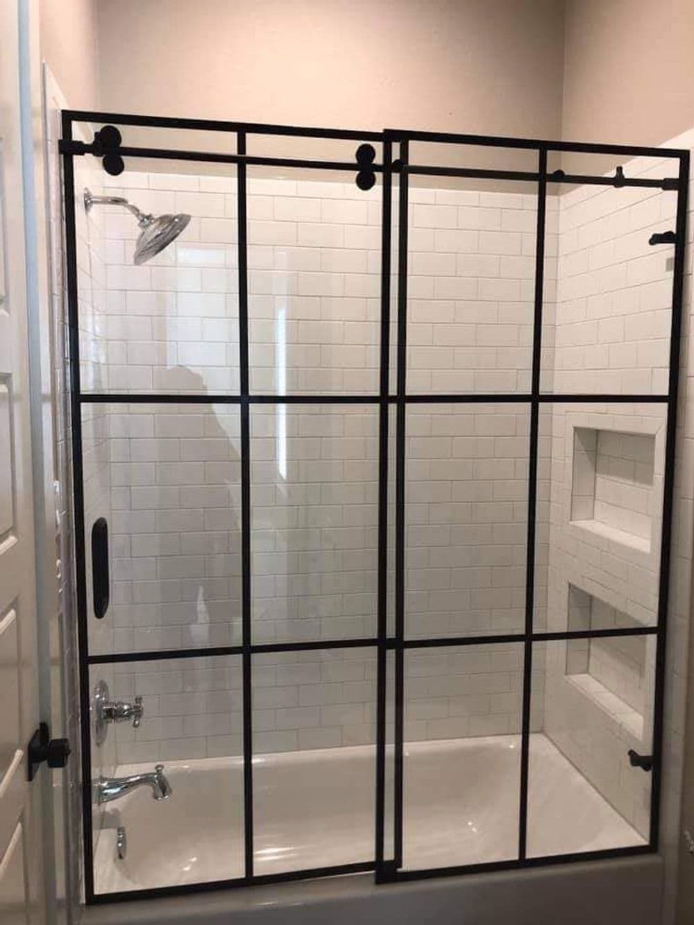 Modern glass shower enclosure with black frames and white subway tile accent wall.