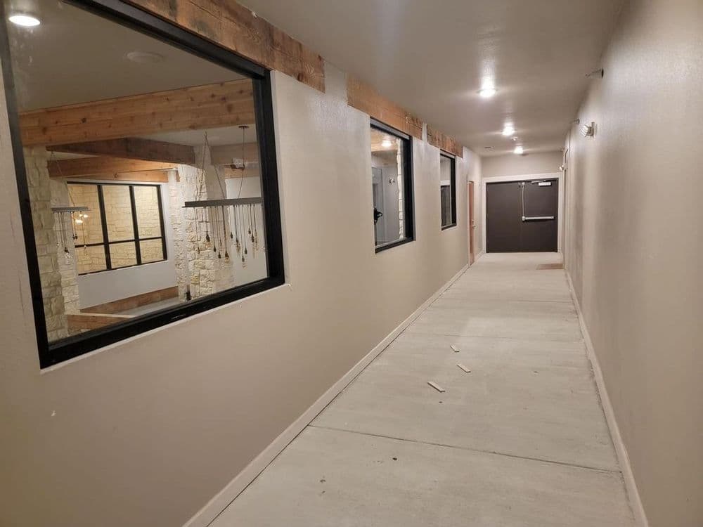 Well-lit hallway with large windows and modern decor, featuring wooden beams and a door at the end.