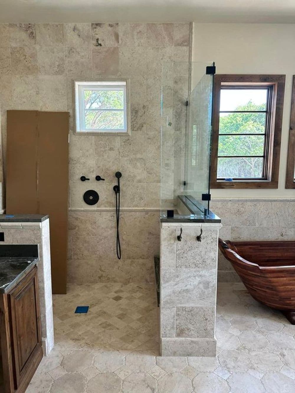 Modern bathroom with stone tiles, walk-in shower, wooden vanity, and freestanding tub.