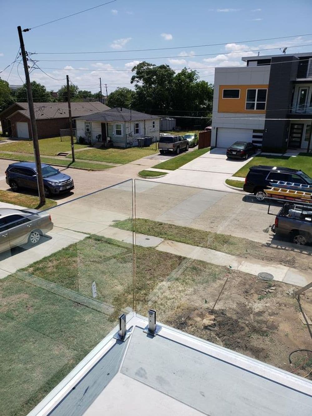 View from a modern balcony overlooking a residential street with cars and houses.