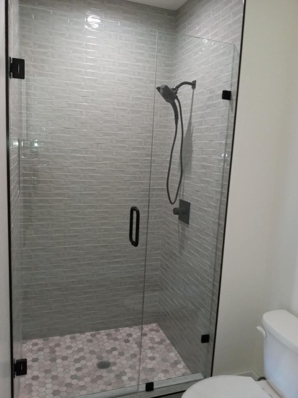 Modern glass shower with gray tile walls, black fixtures, and a decorative tile floor.