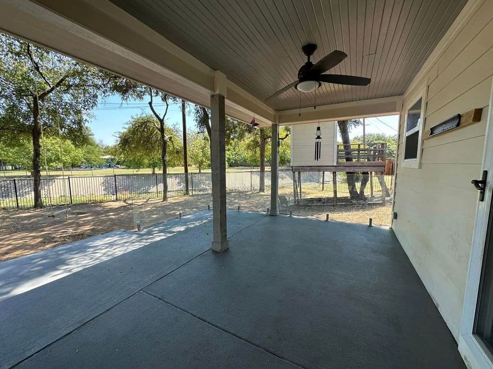 Spacious porch with ceiling fan and access to a backyard playground in a serene setting.