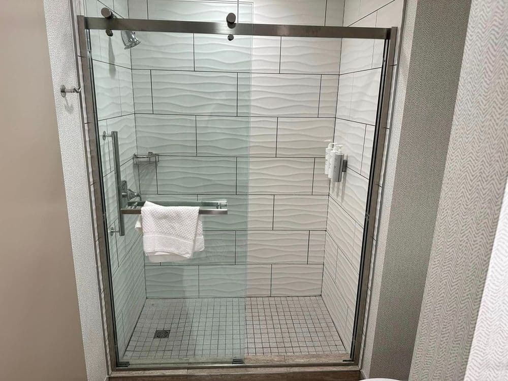 Modern glass shower with textured tiles and a white towel hanging inside.