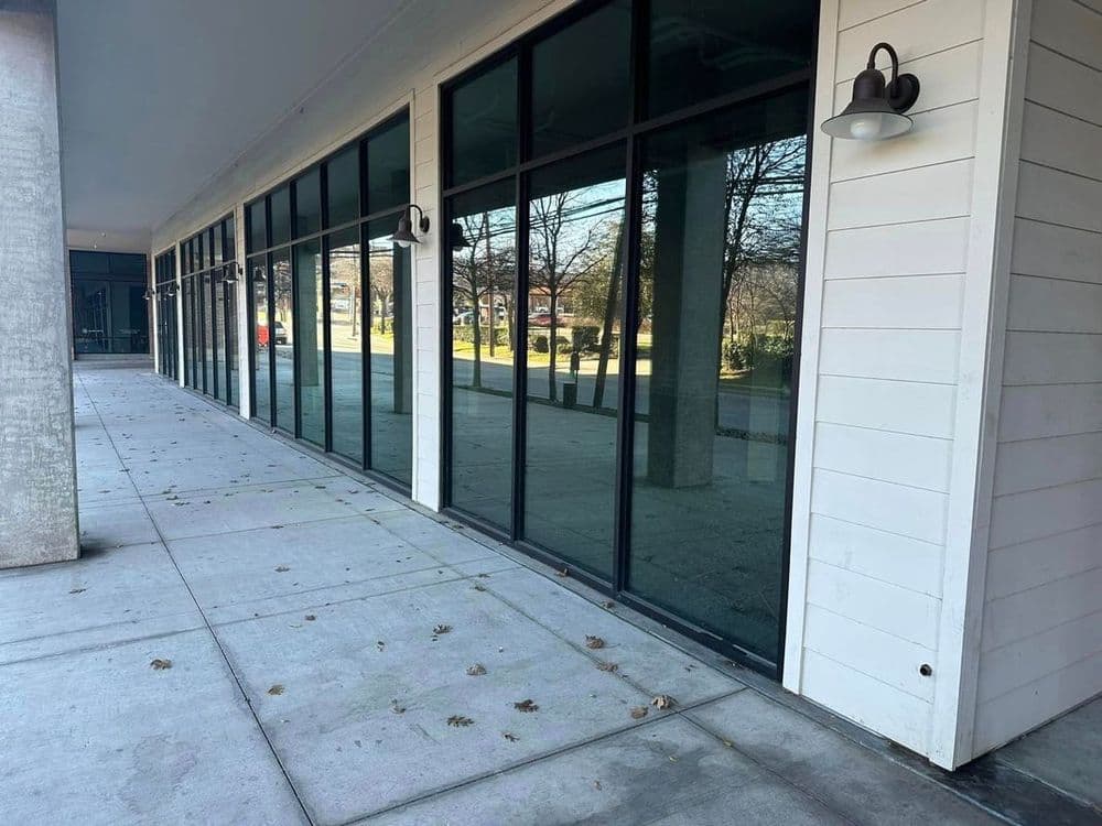 Modern storefront with large glass windows and clean sidewalk, surrounded by trees.