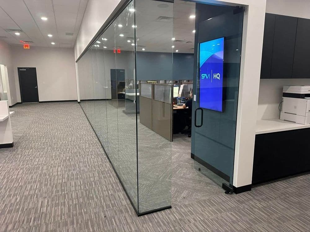 Modern office interior with glass walls, tech workspace, and digital screen display.