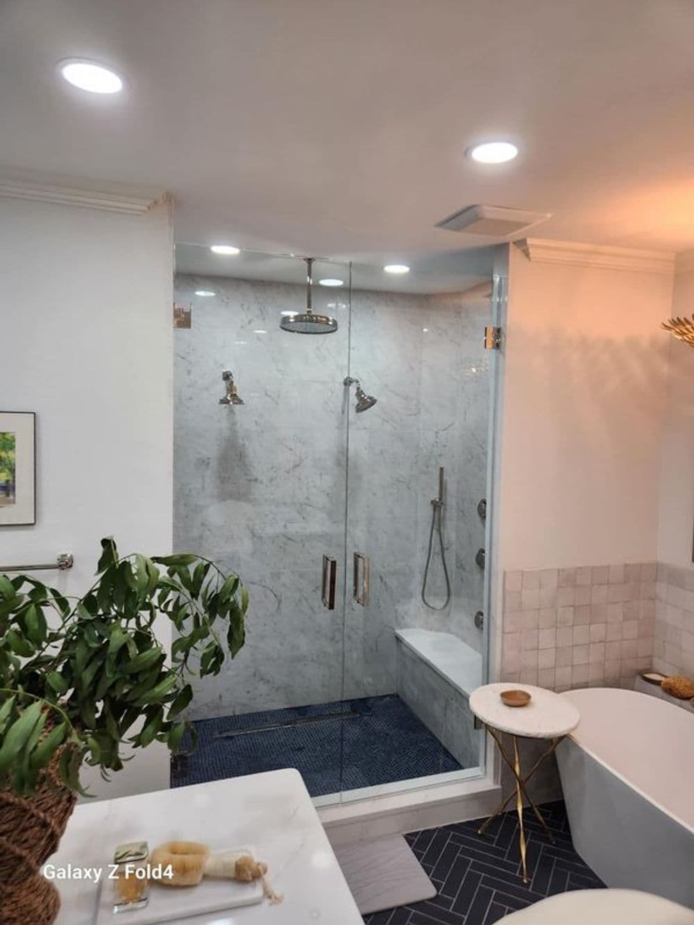 Modern bathroom with glass shower, marble walls, and freestanding bathtub. Natural light.