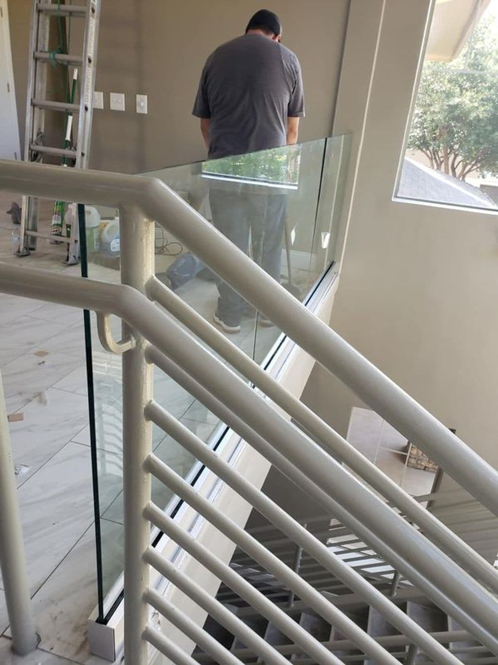 Man installing a modern glass railing in a well-lit interior staircase.